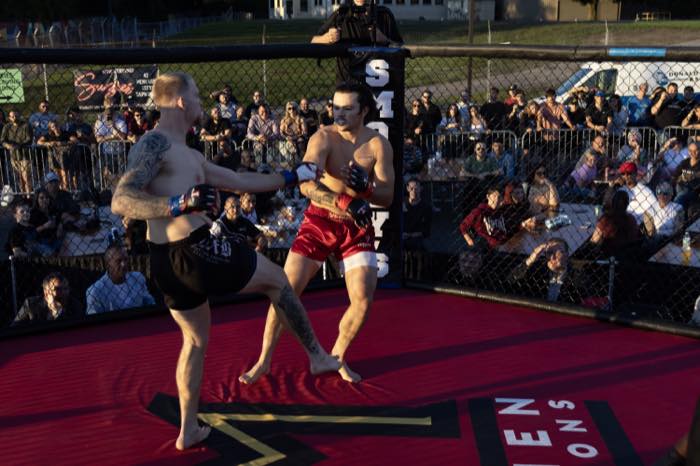 Two mixed martial arts fighters exchanging kicks in an outdoor cage